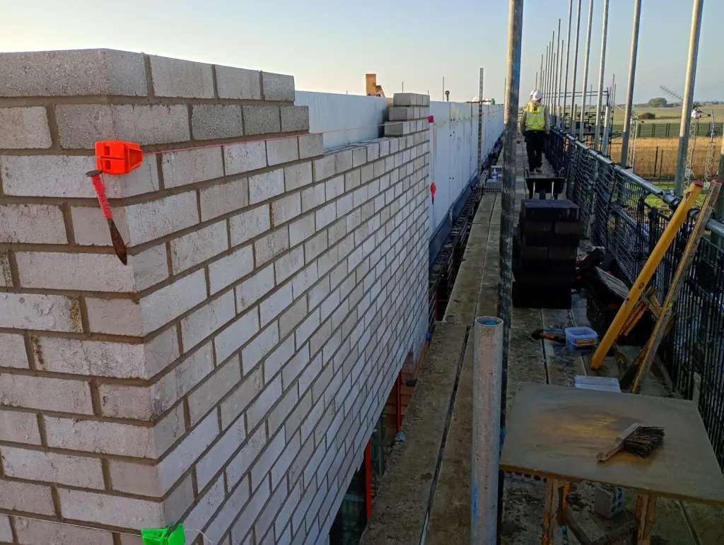 Corner of a buff facing brick wall on scaffold, with a profile and string line set for the next course