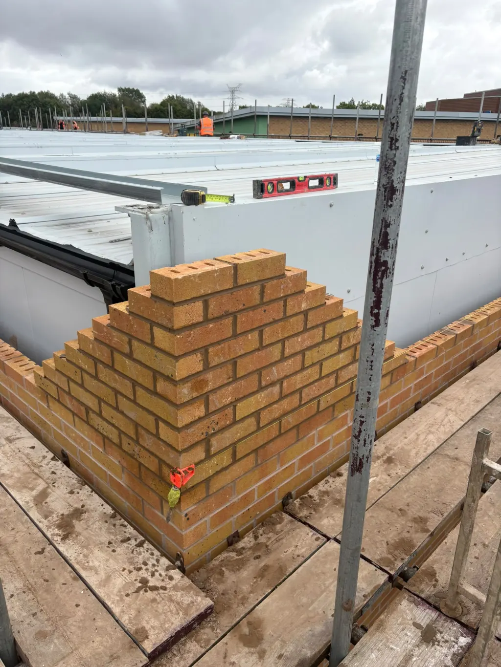 Corner of buff facing brick racked back on the scaffold against white wall panels, with a spirit level on top