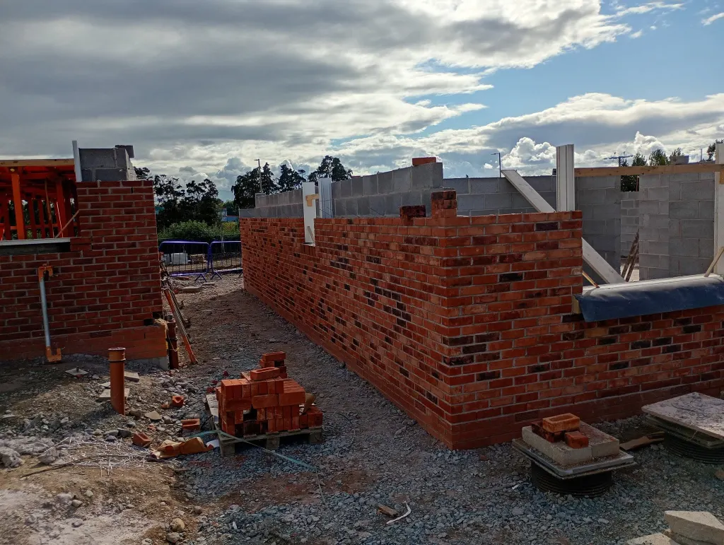 Long run of red facing brick with a blockwork inner leaf and a window opening, bricks loaded out on the gravel