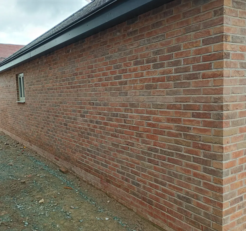 Long side wall of a bungalow in clean red facing brick with air bricks near the base and a single small window