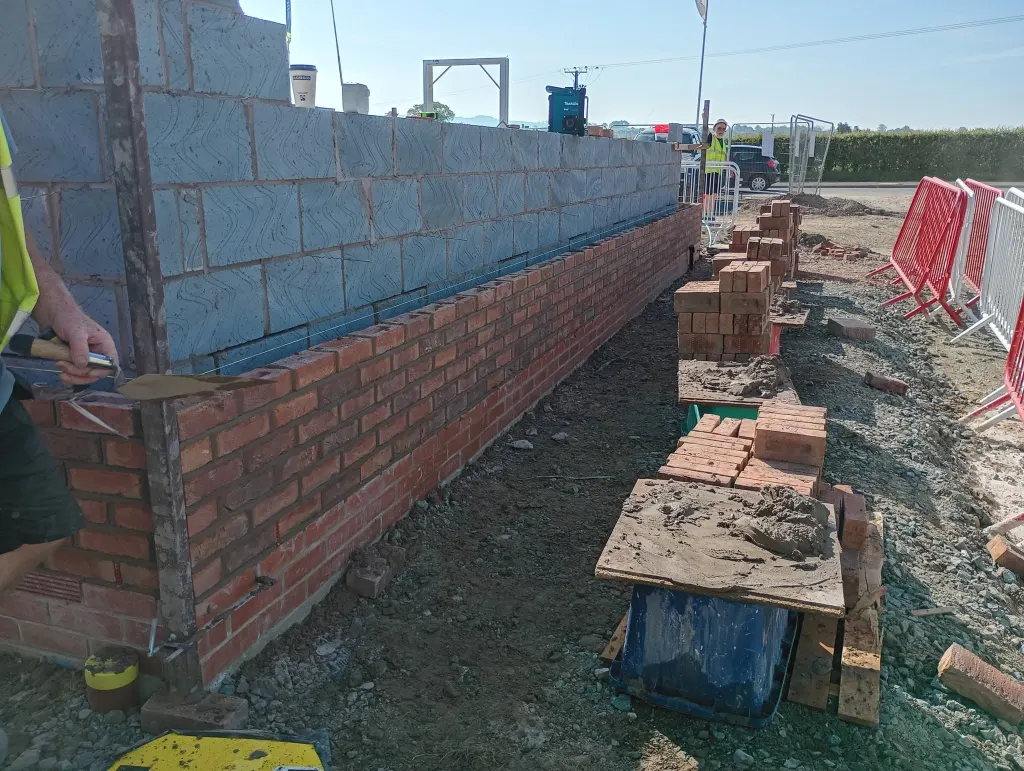 Facing brick outer leaf and grey blockwork inner leaf with the cavity between, and brick piles on the ground alongside