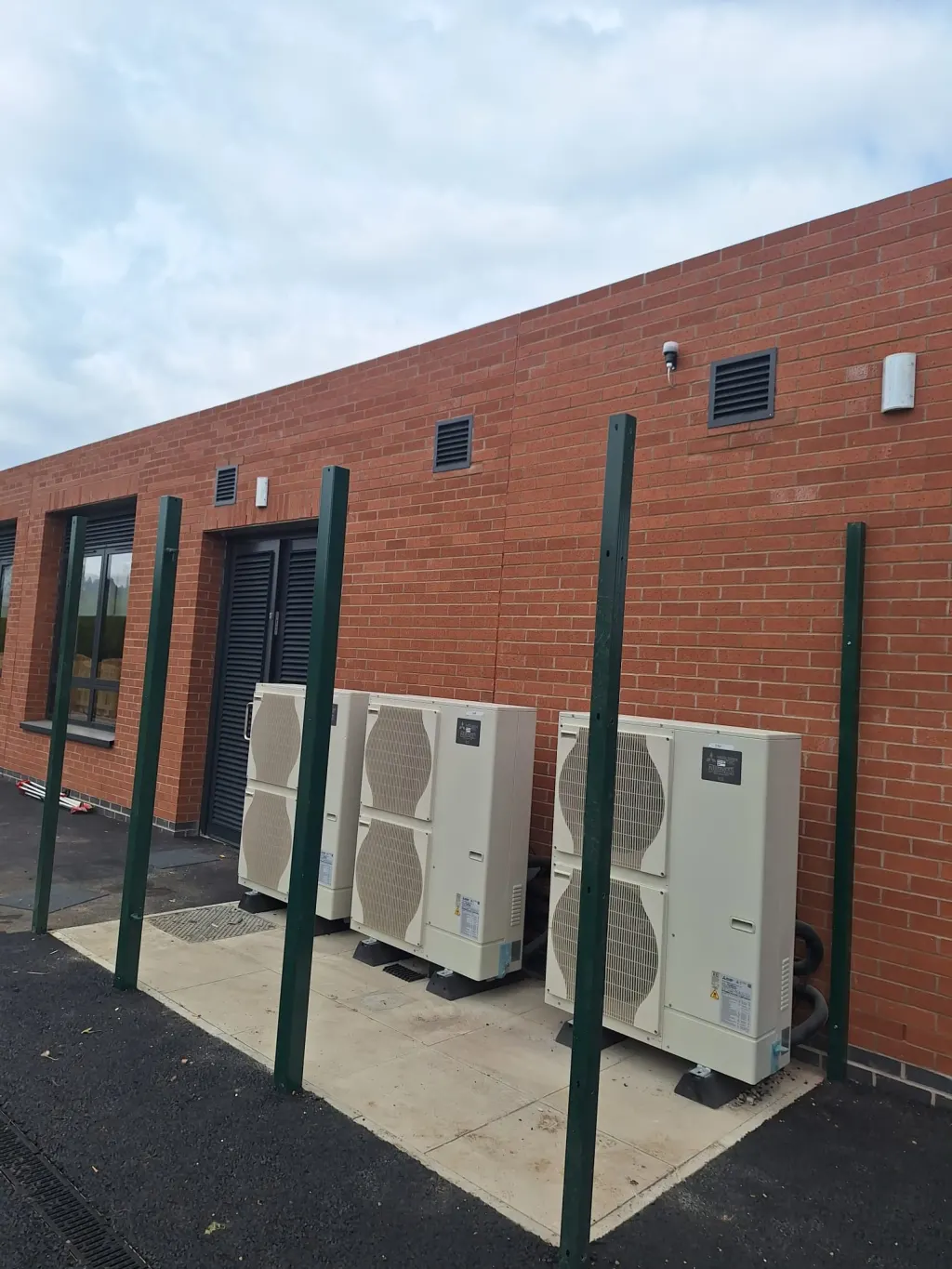 Red facing brick elevation with a louvred door and vents, heat pump units standing on a concrete pad in front
