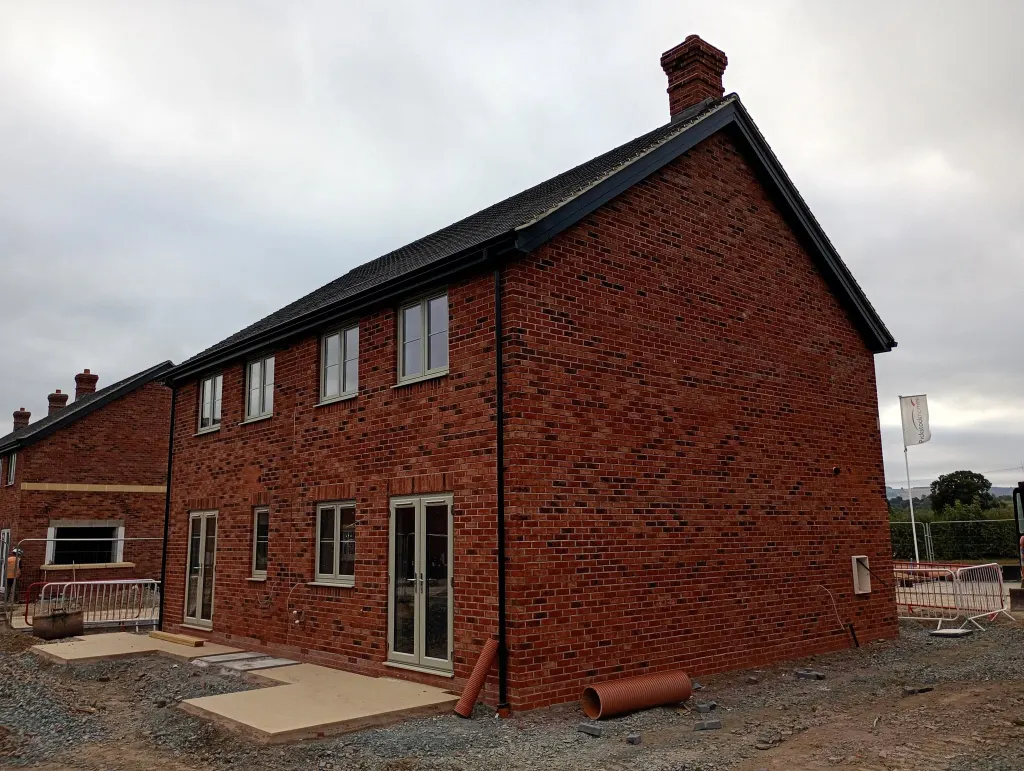 Rear of a semi-detached pair in multi red brick with French doors, cream windows and a chimney on the ridge