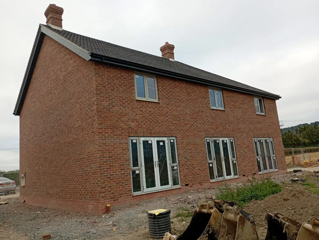 Rear and gable of a two-storey brick pair with a chimney, French doors and bi-fold doors, digger bucket in front