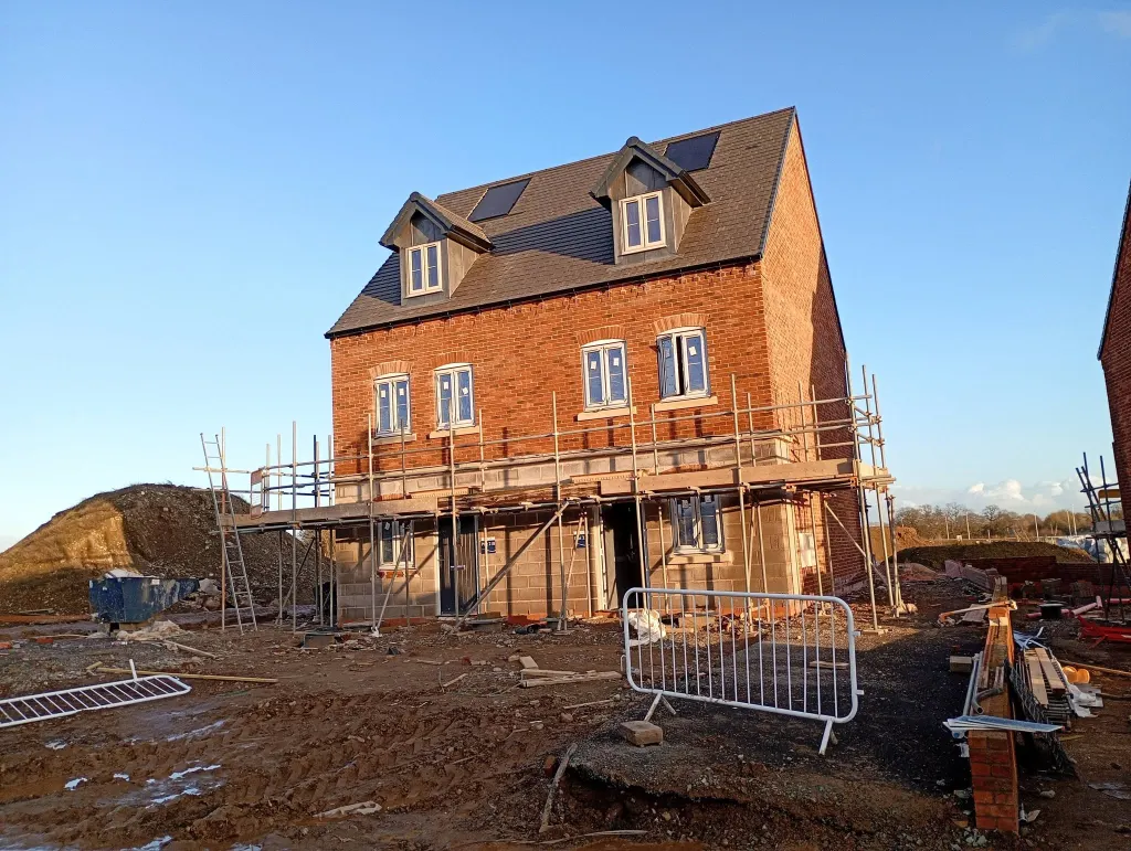 Front of a three-storey red brick townhouse with two dormers, roof windows and scaffold across the ground floor