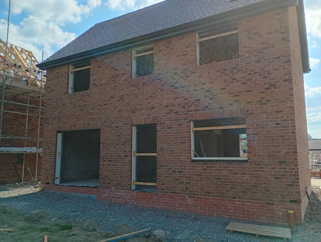 Rear of a two-storey house in multi red facing brick with a tiled roof, large patio opening and empty window openings